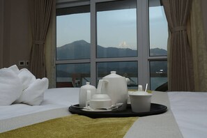 A hotel room with a bed, a tray with tea and cups, and a view of mountains through large windows. - Kings Hotel Rajkuti (Pokhara)