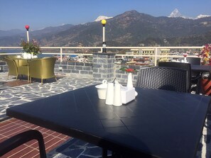 A terrace with a table and chairs, a stone wall, and a view of mountains.