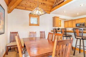 Une table à manger en bois, avec six chaises, un luminaire suspendu et des meubles de rangement en bois dans un coin cuisine.