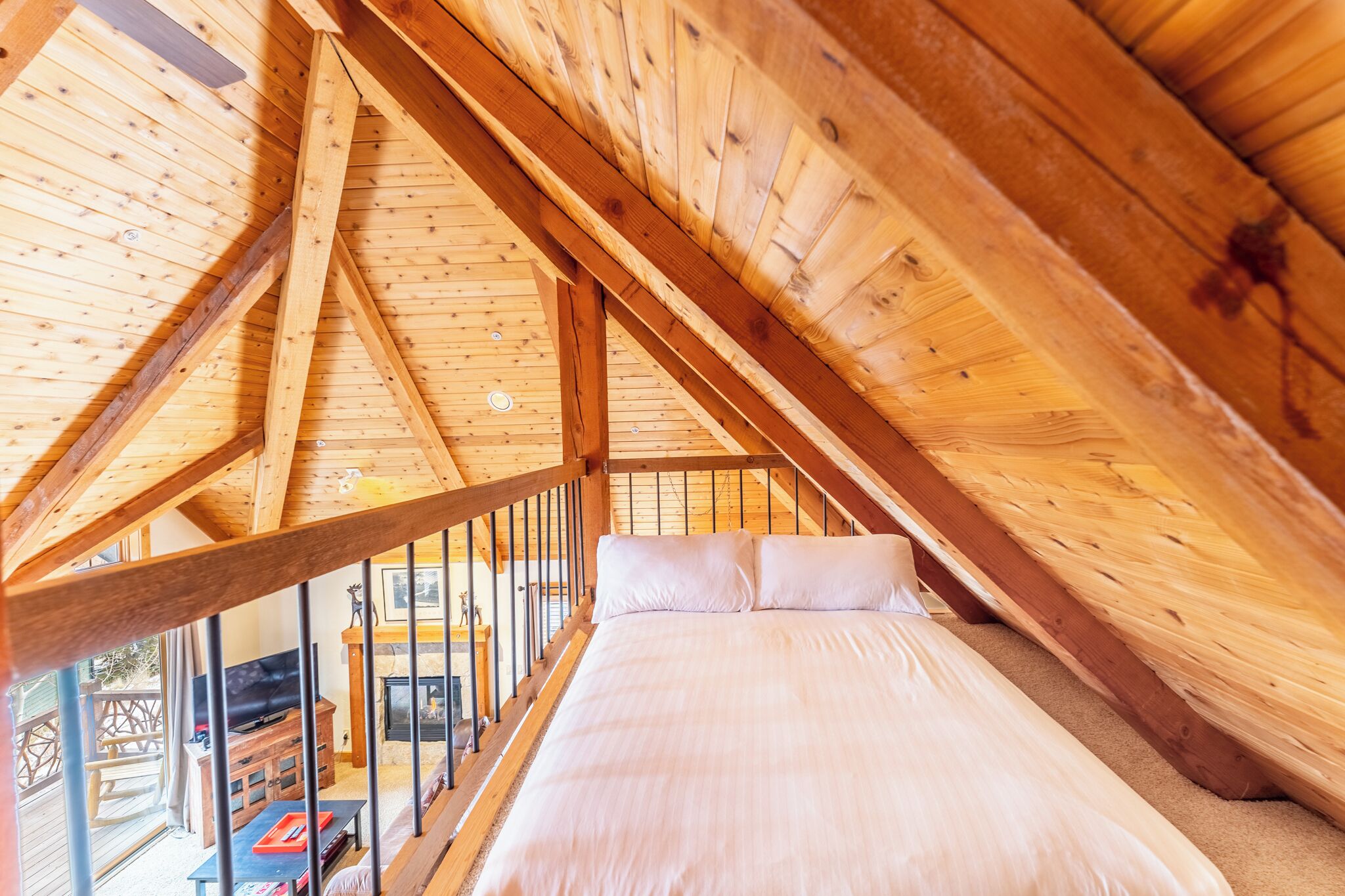 Un dormitorio en el ático con techo de madera, una cama y un televisor.