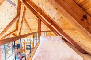 A bedroom with a wooden ceiling, a bed with white bedding, and a view of the outside.
