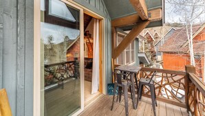 A wooden deck with a table and chairs, a glass door leading to a room, and a view of neighboring houses. - Cabins in the Pines #12 by Summit County Mountain Retreats (Keystone)