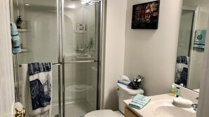 Ein Badezimmer mit Duschkabine, Toilette, Waschbecken mit Toilettenartikeln und einem Spiegel, der den Raum widerspiegelt.