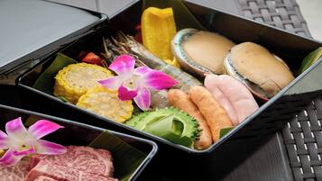 A tray with various food items including corn, shrimp, and a bun, arranged on a woven mat.