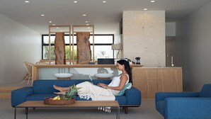 A modern living room with a blue sofa, a coffee table with fruits, and a kitchen area in the background. - ADAN RESORT Sky Villa luxury Suite (Motobu)