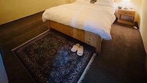 A bedroom with a wooden ceiling, a bed with white bedding, a nightstand with a lamp, and a patterned rug. - The Vintage Guest House Skardu  (Skardu)