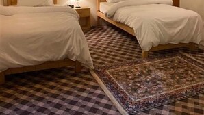 A room with two beds, a checkered floor, a ceiling fan, and a painting on the wall. - The Vintage Guest House Skardu  (Skardu)