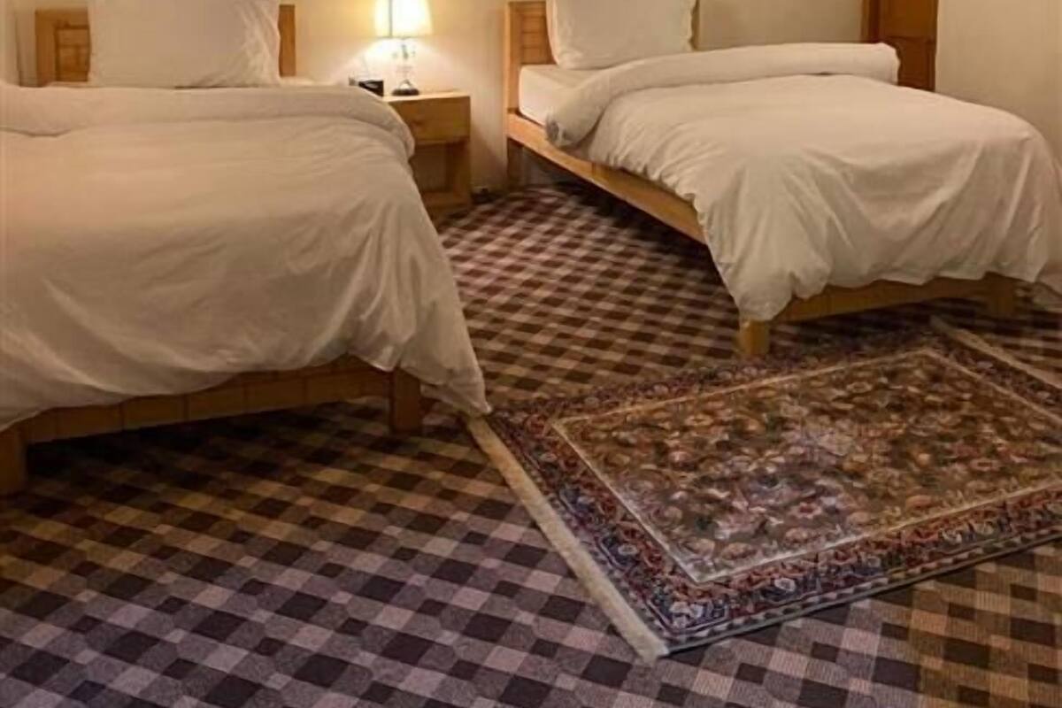 A room with two beds, a checkered floor, a ceiling fan, and a painting on the wall.
