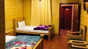 Quarto de hotel pequeno e individual, com uma cama, uma cadeira, uma escrivaninha e uma televisão na parede.