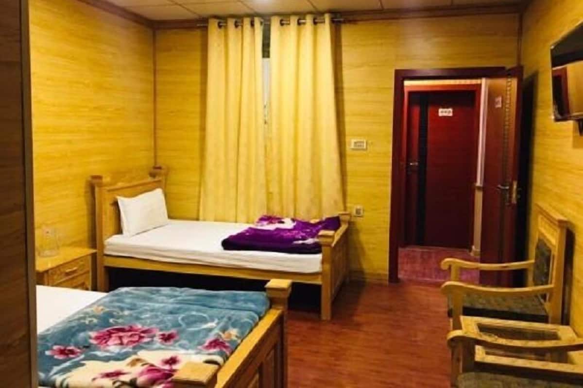 Pieni hotellihuone, jossa on yksi huone, sänky, tuoli, työpöytä ja seinälle asennettu televisio.