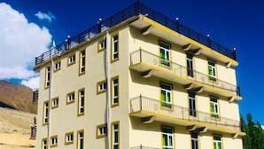 Um edifício com várias andares, varandas, telhado plano e montanhas ao fundo.