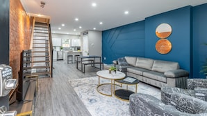 Una sala de estar moderna con un sofá gris, dos espejos redondos, una mesita de centro y una escalera con barandilla de metal.