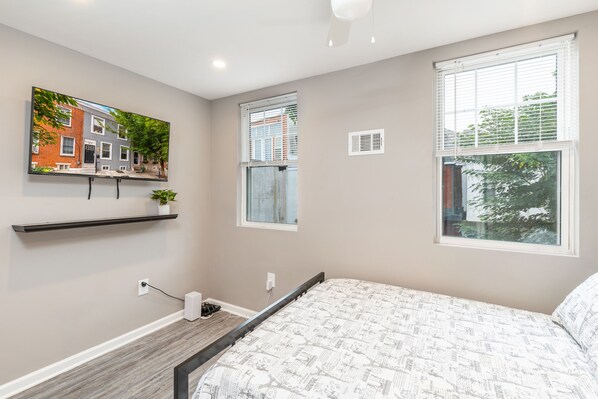 A bedroom with a bed, a painting of a building, a window, and a shelf. - New, Beautiful Home in the Heart of Philly!!! (Philadelphia)