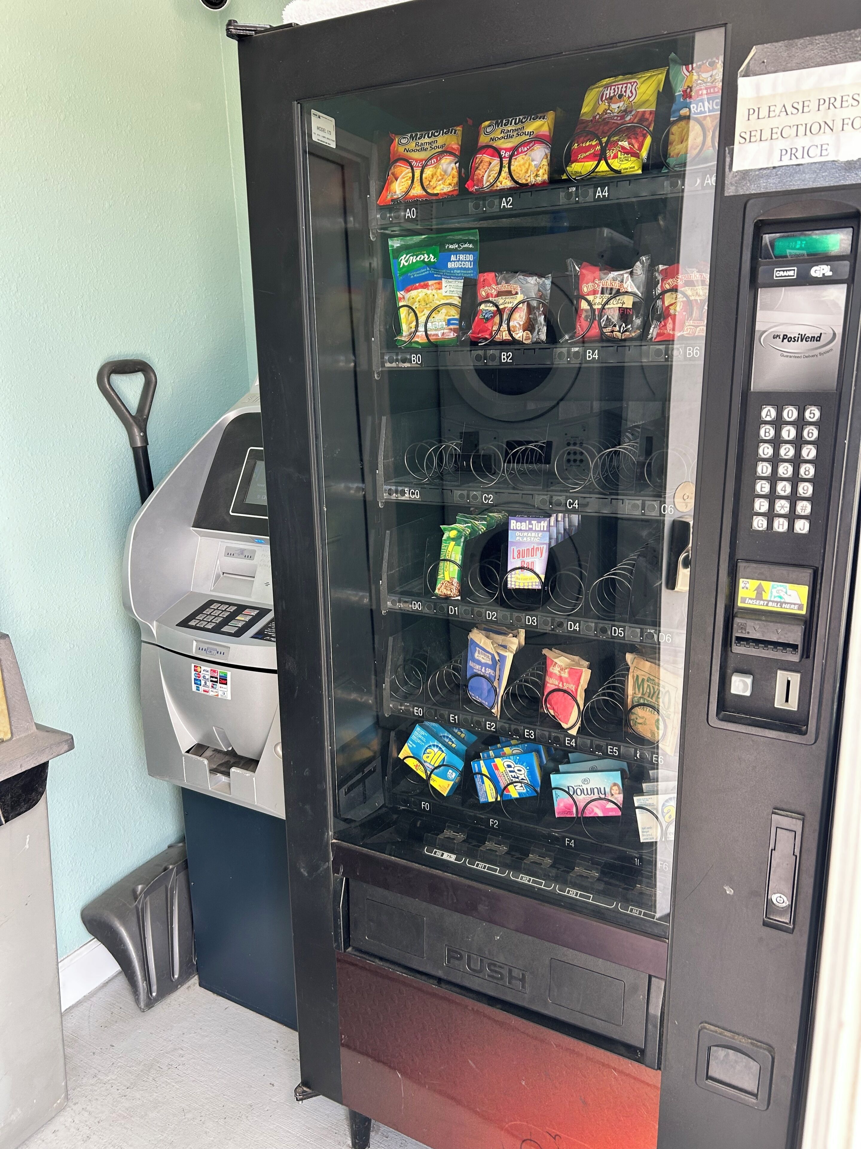 Máquina de vendas com diversas opções de lanches, um terminal de pagamento e um aviso indicando a seleção por preço.