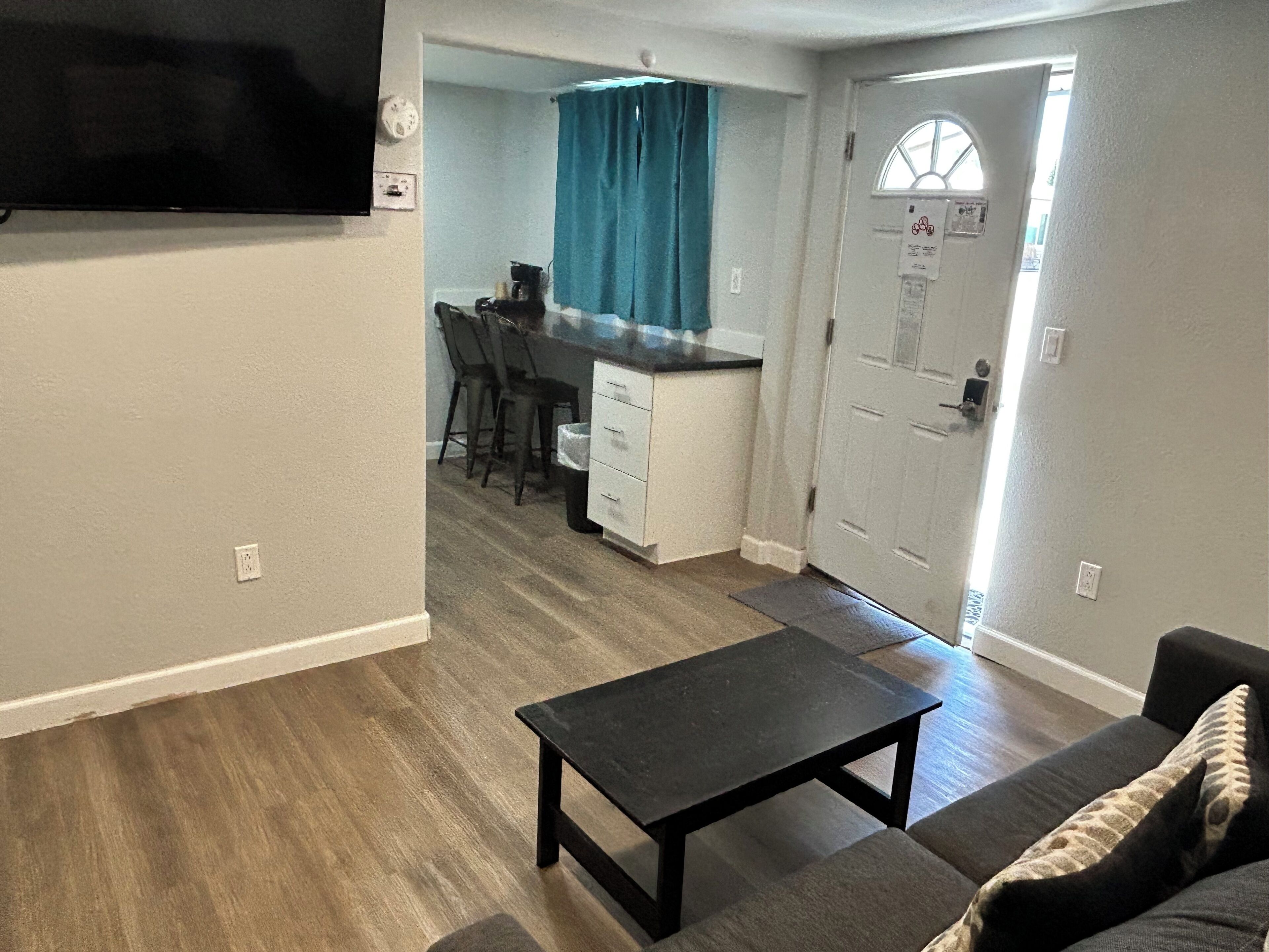 A living room with a black coffee table, a gray sofa, and a kitchen area with a bar and chairs.