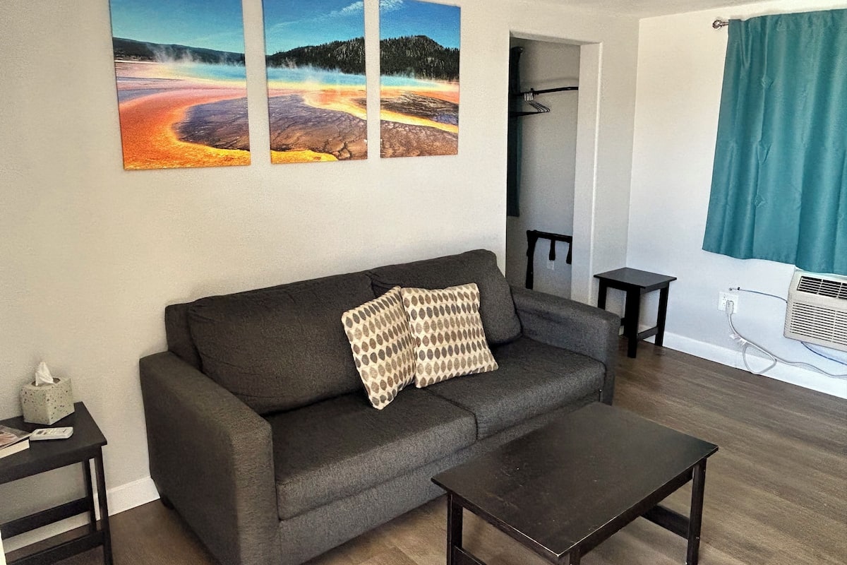 A living room with a sofa, a coffee table, and three paintings on the wall.