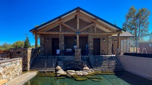 A building with a stone facade, a clear pool with rocks, and a staircase leading to the entrance.