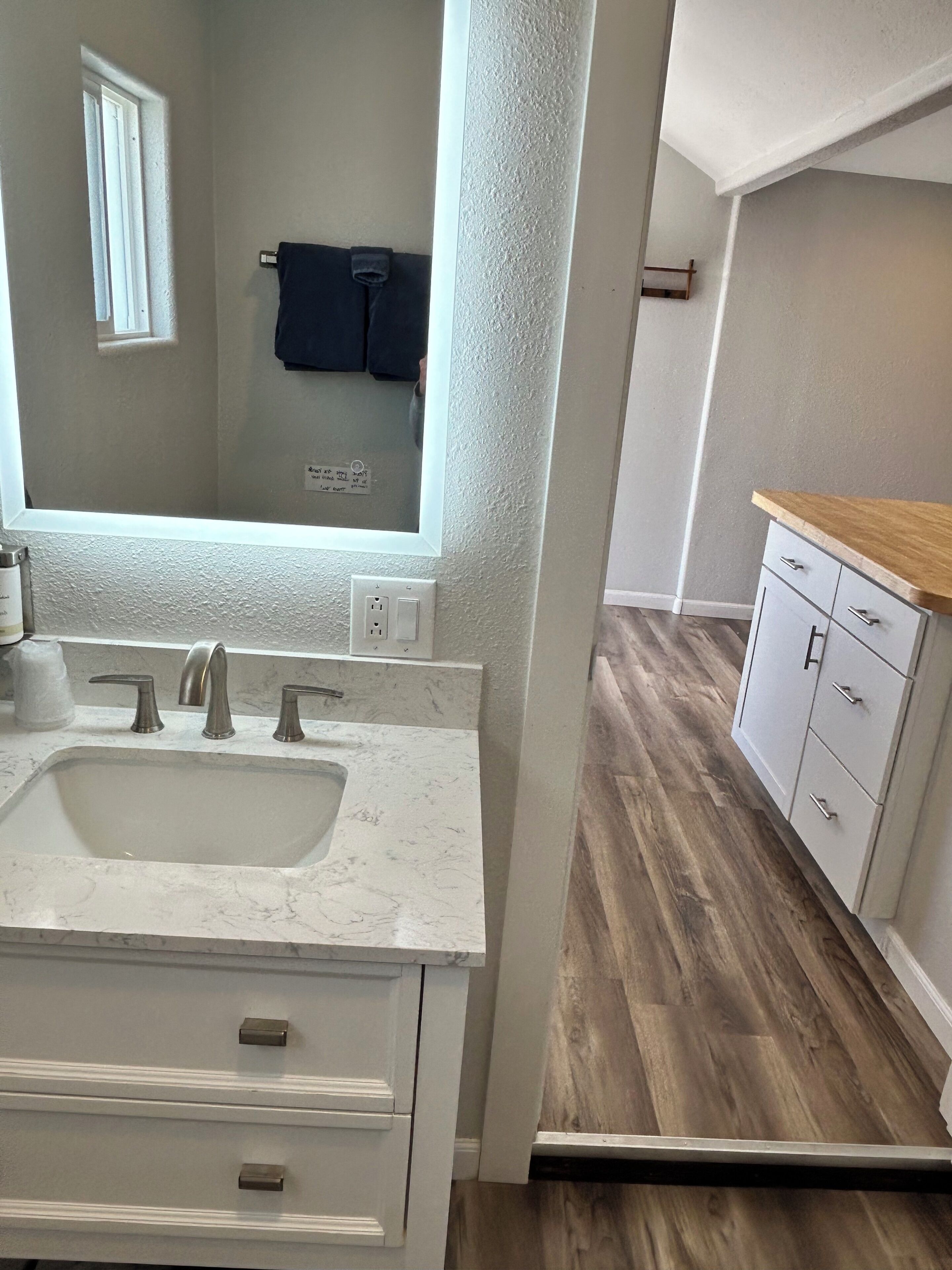 A bathroom with a white sink, two faucets, and a mirror. There is a wooden cabinet with drawers and a countertop.