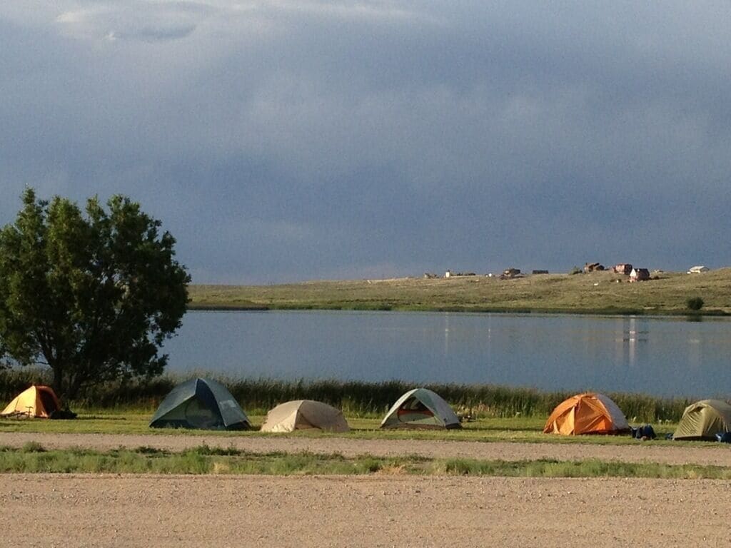 A lakeside camping area with multiple tents and a large tree.