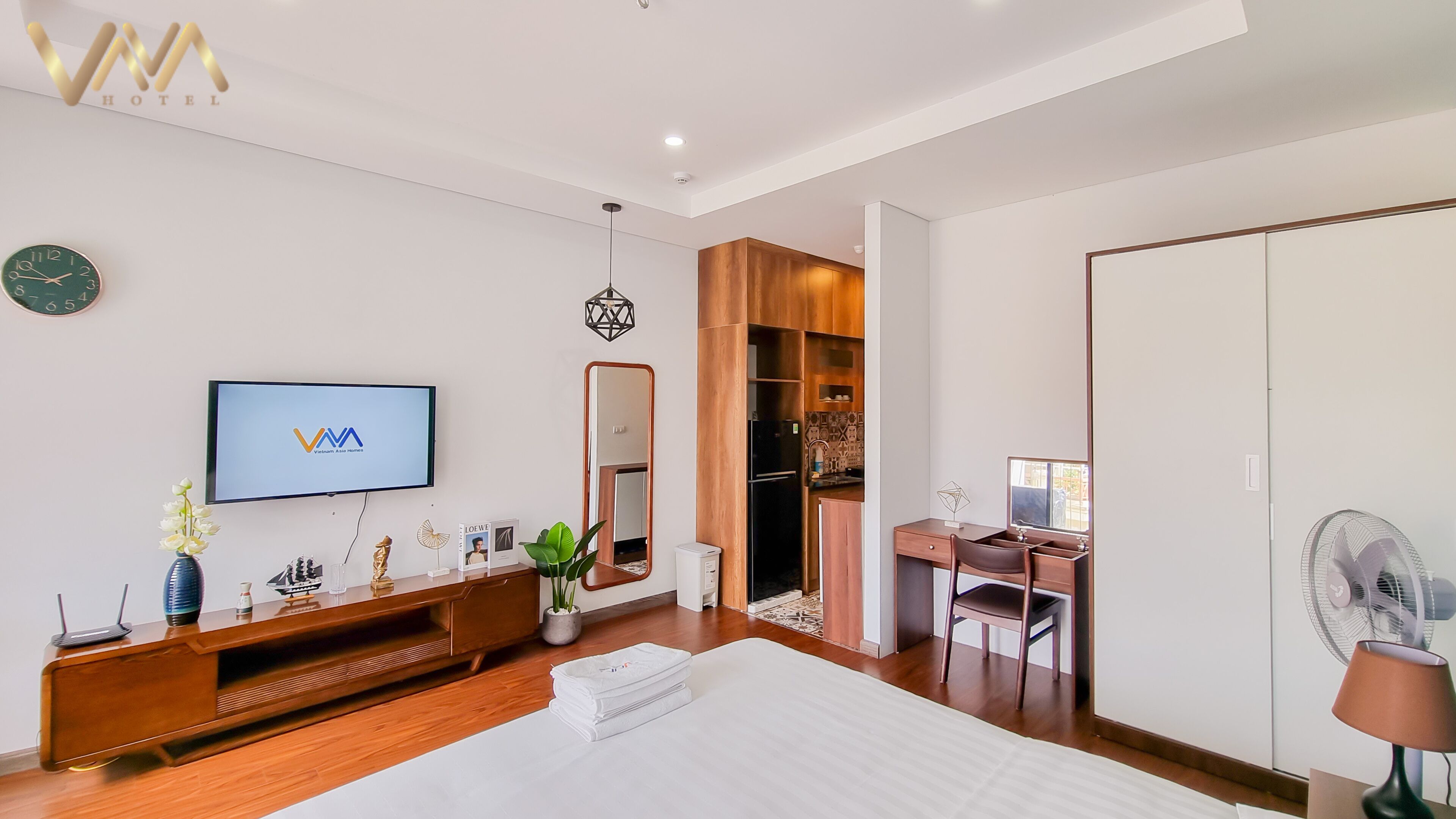 A modern hotel room with a large bed, a TV, a wooden desk, a wardrobe, and a bathroom.
