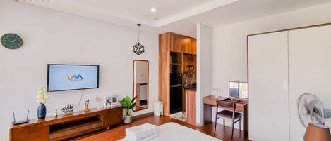 A modern hotel room with a large bed, a TV, a wooden desk, a wardrobe, and a bathroom.