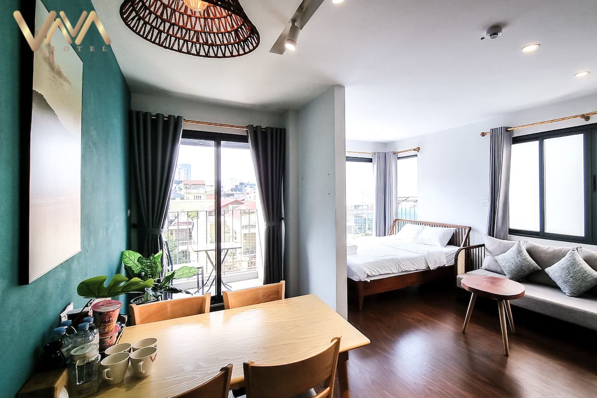 Une chambre d’hôtel moderne avec une table à manger en bois, un canapé, un lit et un balcon offrant une vue sur la ville.