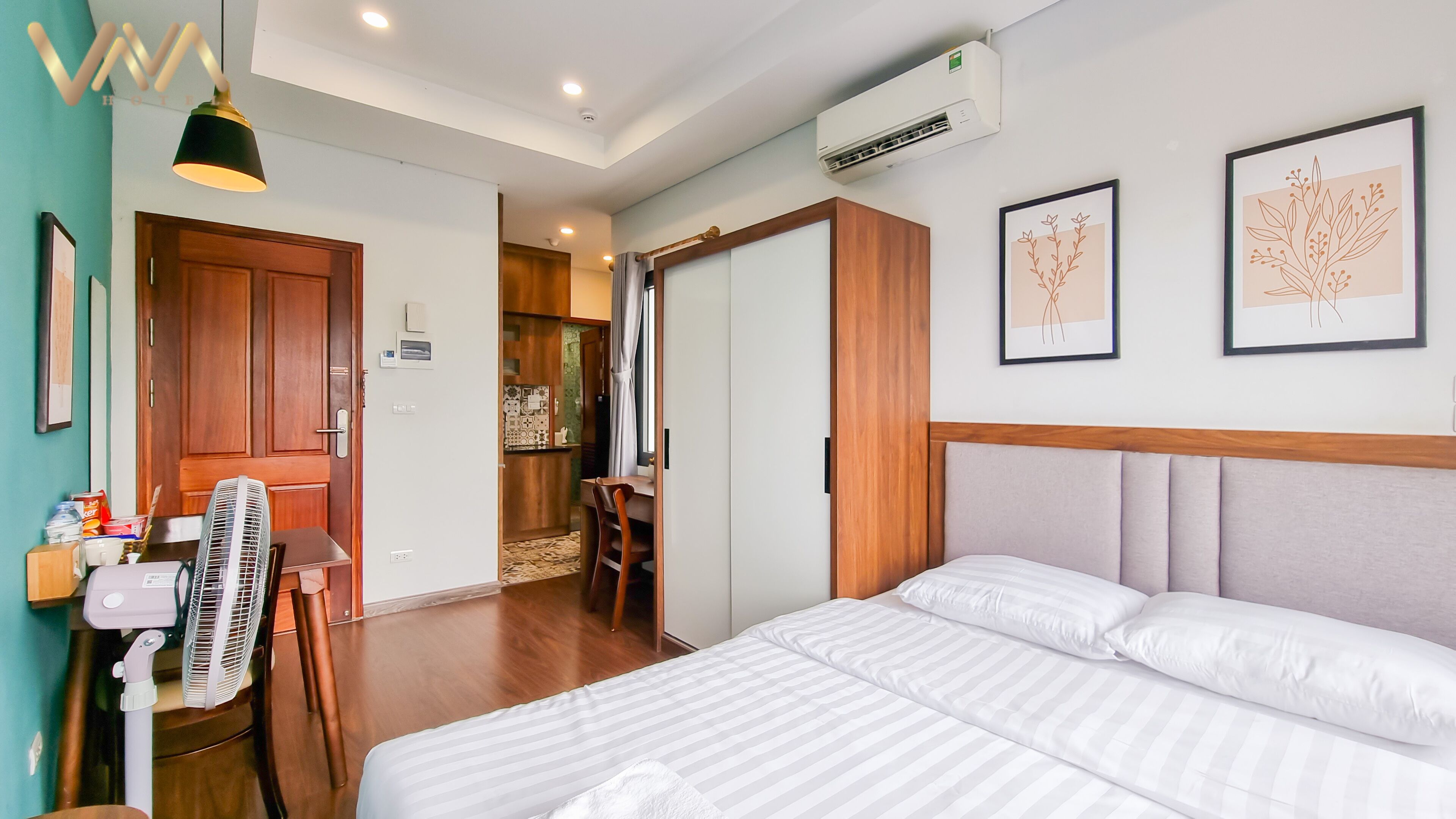 A hotel room with a bed, a desk, a chair, an air conditioner, and a window.