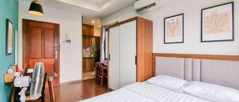 A hotel room with a bed, a desk, a chair, an air conditioner, and a window.