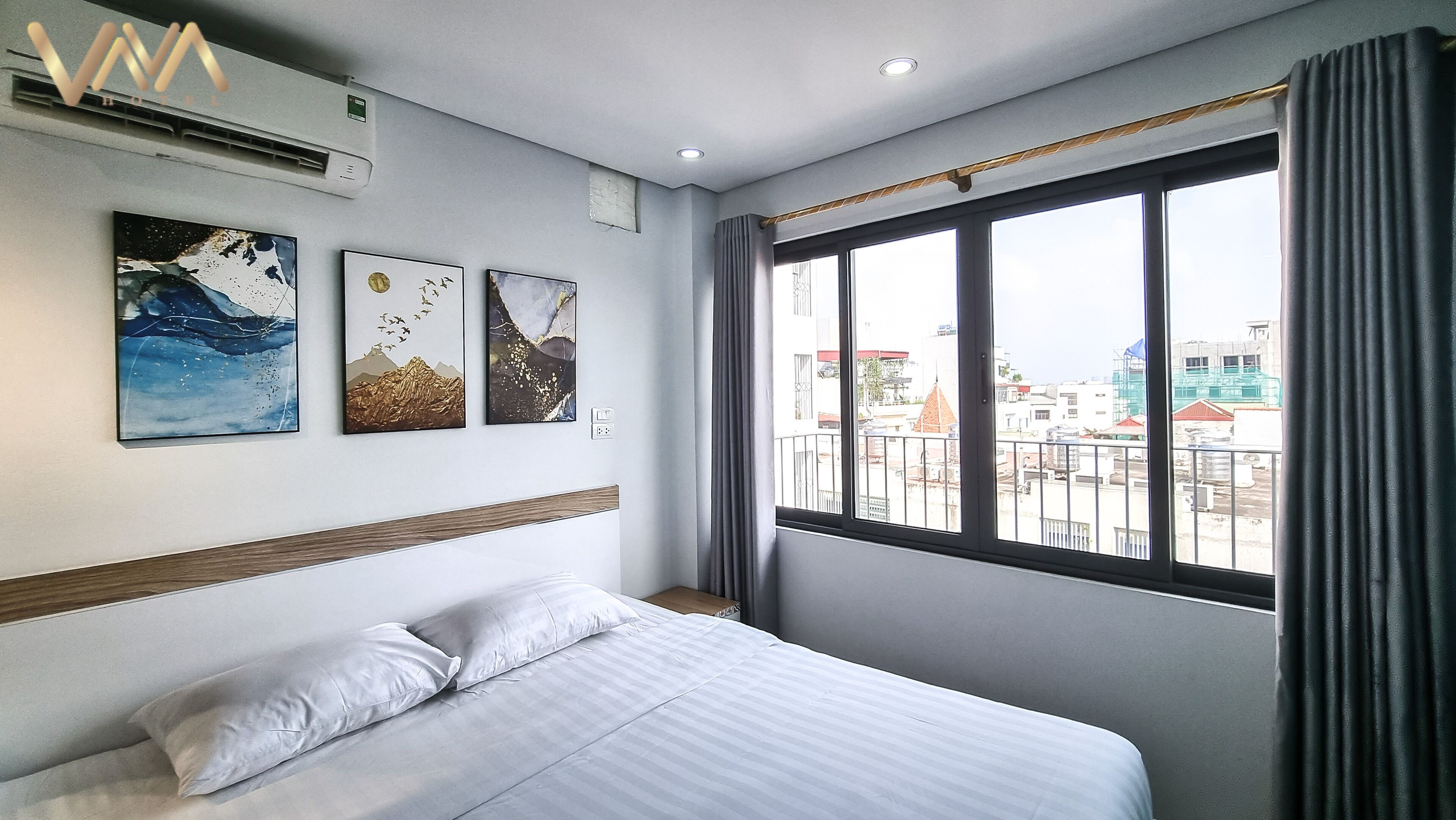 Une chambre d’hôtel avec un lit, une grande fenêtre avec des rideaux et trois œuvres d’art accrochées au mur.