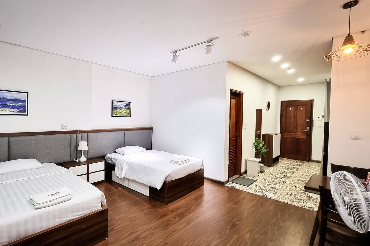 Une chambre d’hôtel avec deux lits, une tête de lit en bois, une table de chevet, une lampe et un ventilateur.