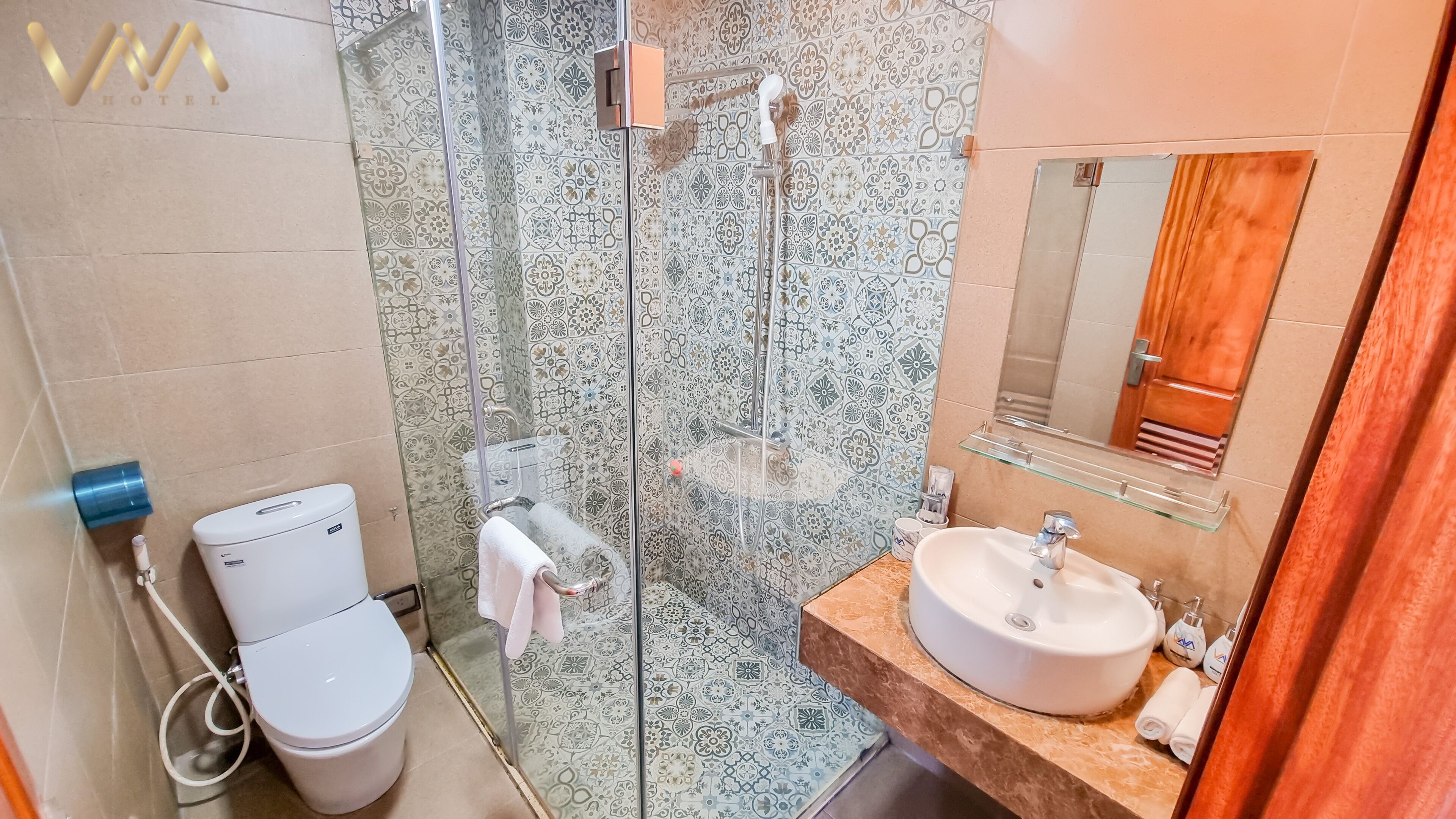 Ein Badezimmer mit Toilette, einer Glasdusche, einem Waschbecken mit Spiegel und gemusterten Fliesen.