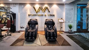 Une salle de sport équipée de deux fauteuils de massage, de matériel d’exercice et d’un mur en marbre sur lequel est inscrit le nom de la salle.