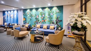 Un hall d’hôtel avec un canapé bleu, des fauteuils beiges, une table basse ronde et un sol à motifs.