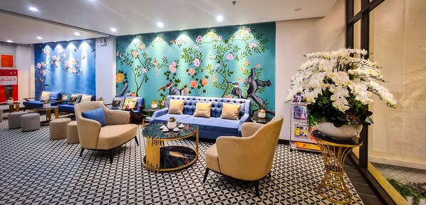Un hall d’hôtel avec un canapé bleu, des fauteuils beiges, une table basse ronde et un sol à motifs.