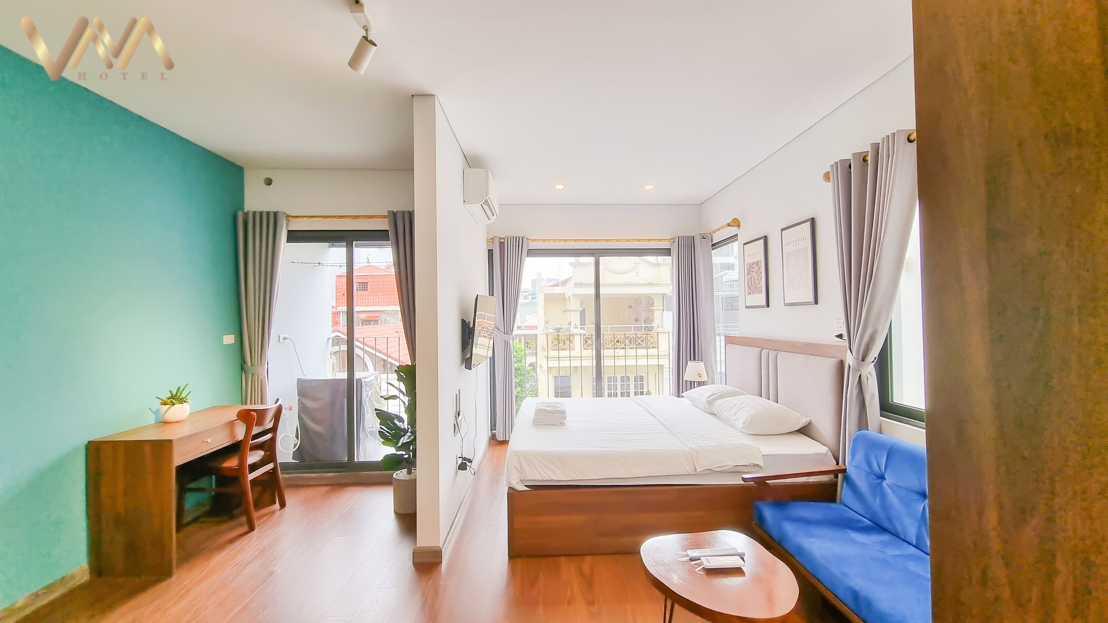 Une chambre d’hôtel avec un lit, un canapé bleu, une petite table, un bureau et une télévision.