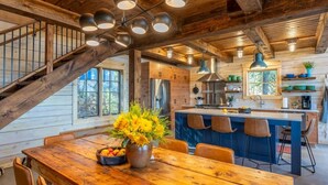 A rustic kitchen with wooden beams, a central island with bar stools, and a dining area with a wooden table and chairs. - Northern Exposure Modern Log Cabin (Ely)