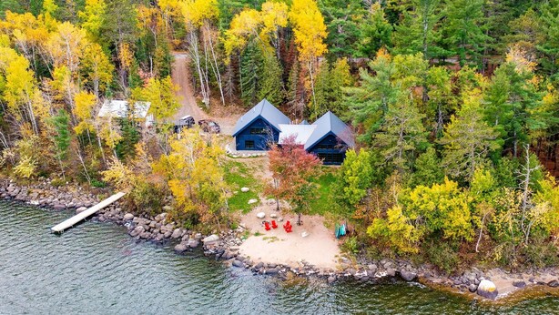 A lakeside cabin with a dock, surrounded by autumn foliage. - Northern Exposure Modern Log Cabin (Ely)