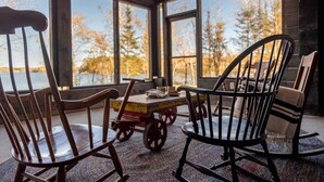 A cozy seating area with a wooden table and chairs, large windows with a view of trees and a body of water. - Northern Exposure Modern Log Cabin (Ely)