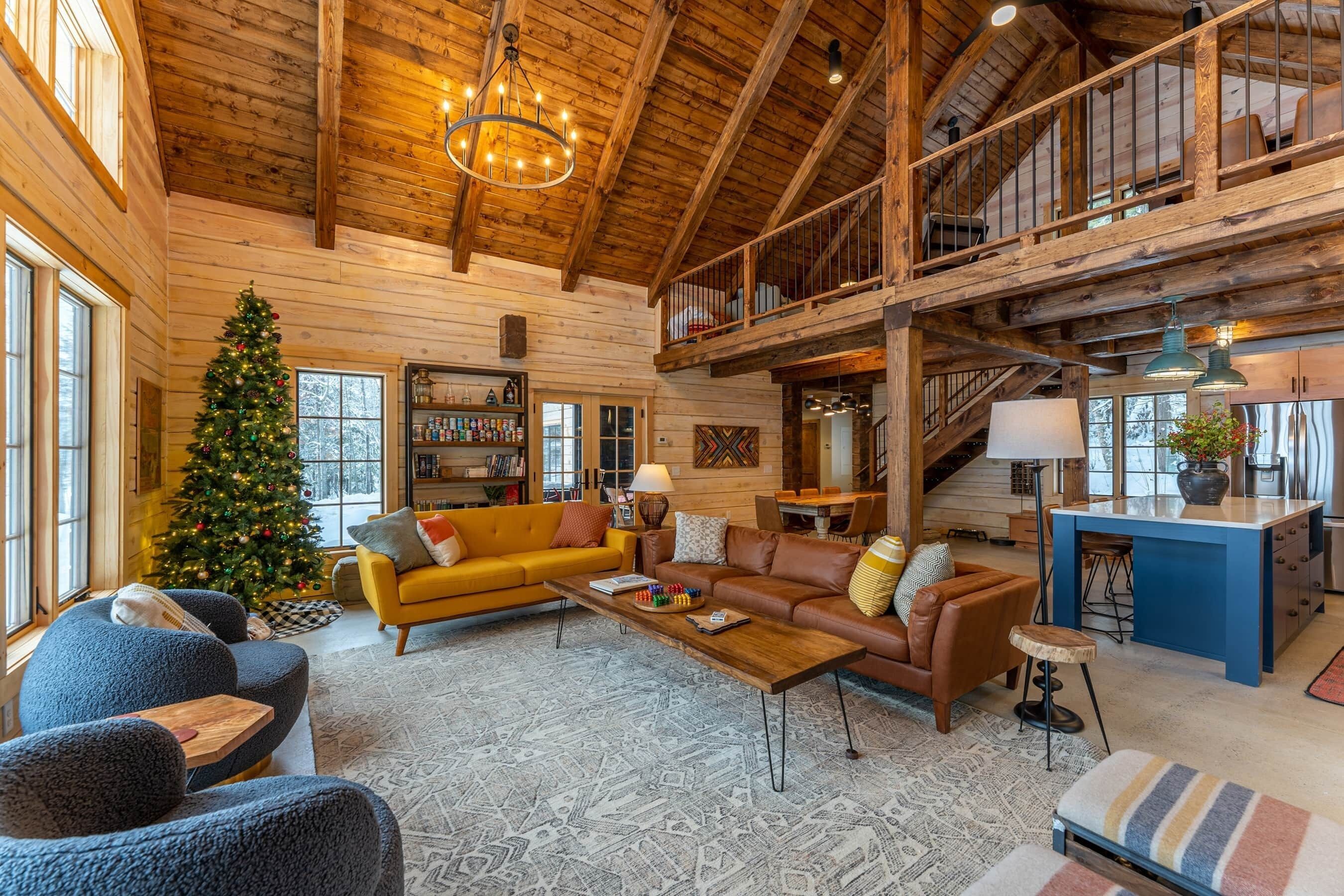 A spacious living area with a high ceiling, wooden beams, a Christmas tree, a sofa, a coffee table, and a kitchen area.
