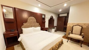 Una habitación de hotel con una cama grande, cabecera de madera, tocador con espejo, una silla y un armario.
