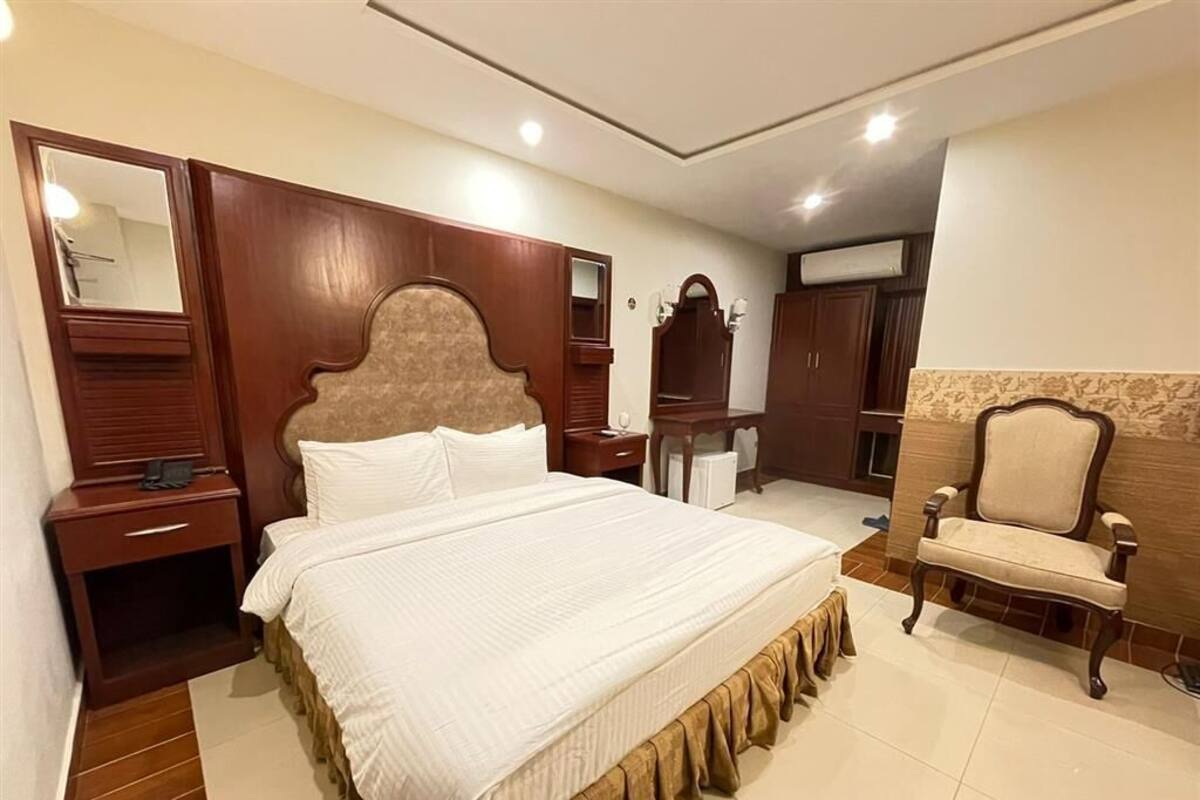 Una habitación de hotel con una cama grande, cabecera de madera, tocador con espejo, una silla y un armario.