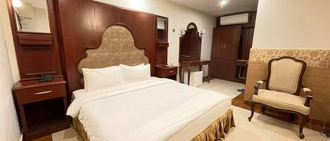 A hotel room with a large bed, wooden headboard, a vanity with a mirror, a chair, and a wardrobe.