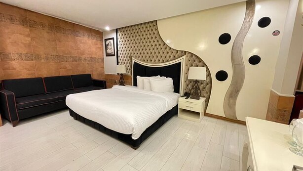 Un dormitorio moderno con una cama grande, un sofá, una mesita de noche y un adorno en la pared.