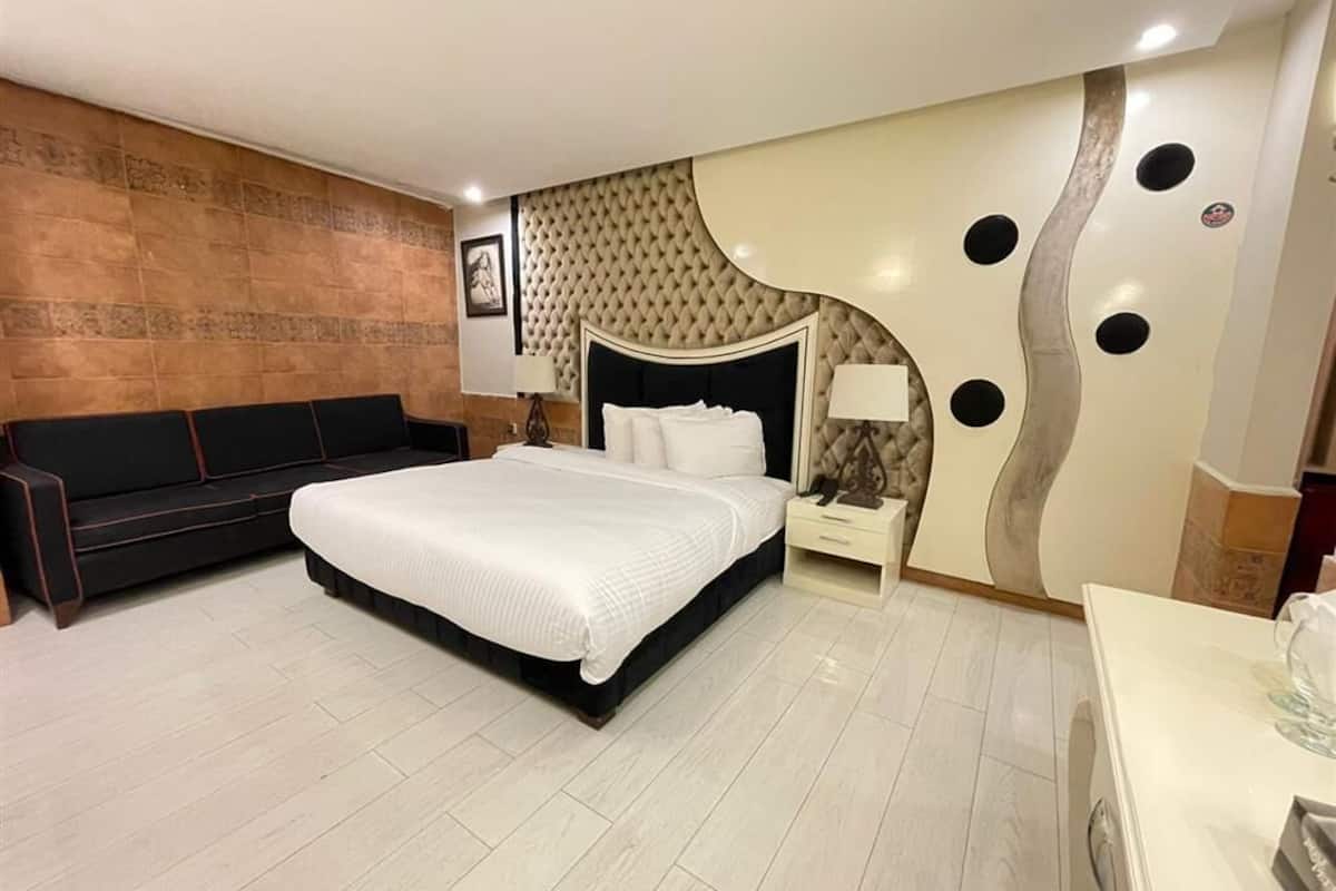 Un dormitorio moderno con una cama grande, un sofá, una mesita de noche y un adorno en la pared.