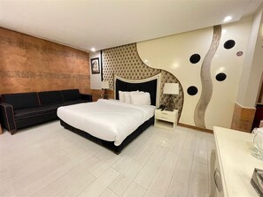 A modern bedroom with a large bed, a sofa, a nightstand, and a decorative wall. - Al Noor Hotel Multan  (Multan)