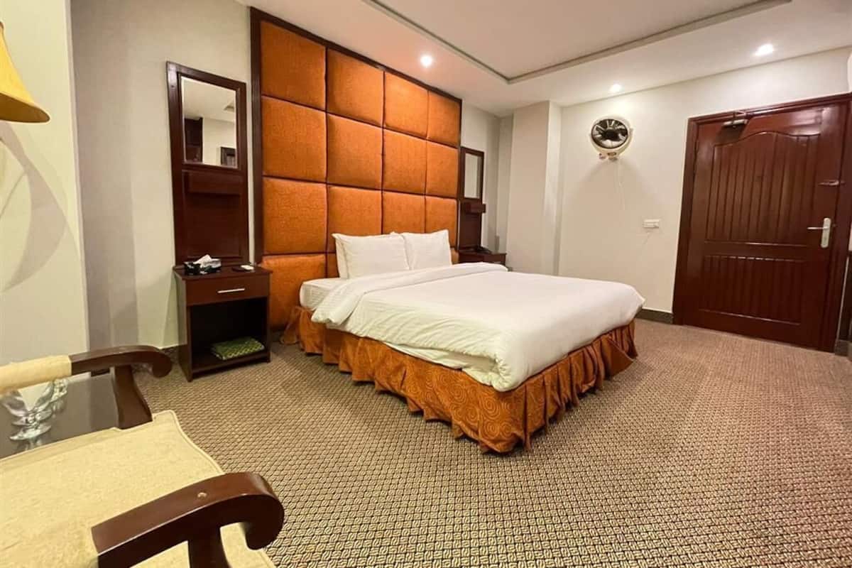 Una habitación de hotel con una cama grande, cabecera de madera, mesita de noche con lámpara y armario.