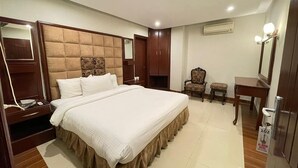 Una habitación de hotel con una cama grande, un armario de madera, una mesita pequeña y una silla.