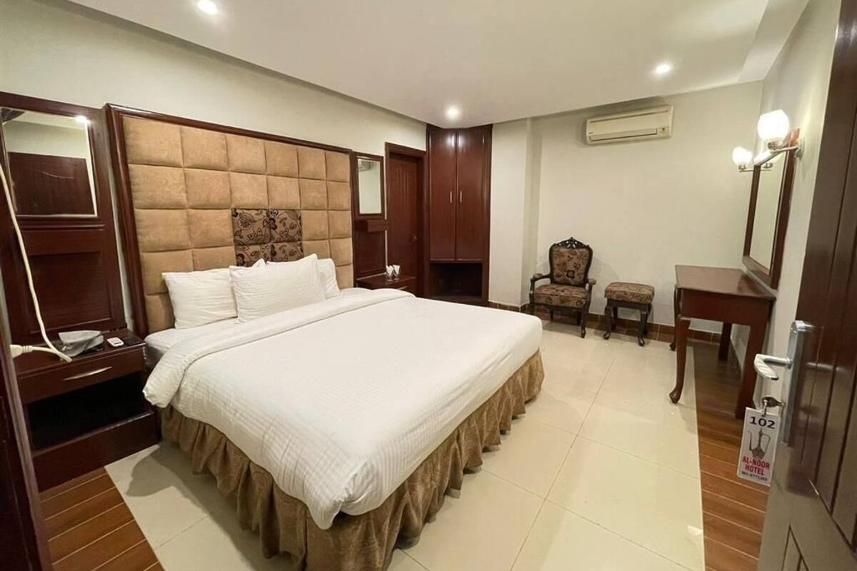 Una habitación de hotel con una cama grande, un armario de madera, una mesita pequeña y una silla.