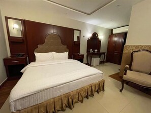 A hotel room with a large bed, a wooden headboard, a nightstand, a chair, a desk, and a mirror.