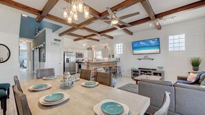 Een ruime keuken met moderne apparatuur, een eetgedeelte met een houten tafel voor vier personen, en een gezellige zithoek met een bank en een aan de muur bevestigde televisie.